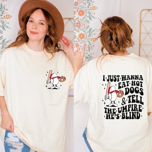 May include: A cream colored t-shirt with a baseball character graphic on the front and the text "I just wanna eat hot dogs & tell the umpire he's blind" on the back.