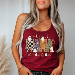 May include: A maroon tank top featuring the word MAMA in large, patterned letters filled with ghosts, pumpkins, bats, and stars. Below the text, the names Oliver, Emily, and Rose are printed in white script, accompanied by small ghost illustrations.