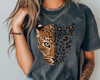 May include: Dark gray t-shirt featuring a half-face leopard design. The leopard's face is detailed with brown and black spots, a yellow eye, and a tan snout. The other half of the design is a pattern of leopard spots. The shirt has short sleeves.