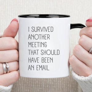 May include: White ceramic coffee mug with a black rim and handle. The mug has the text "I survived another meeting that should have been an email" printed on it.