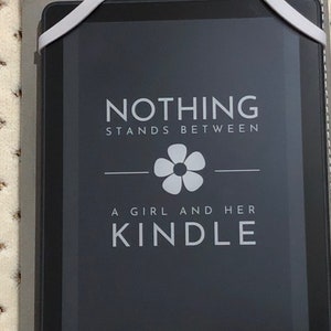 May include: A black and white image of an e-reader with the text "NOTHING STANDS BETWEEN A GIRL AND HER KINDLE" on the screen.
