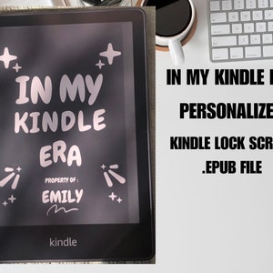 May include: A black and white Kindle e-reader with a personalized lock screen that says "In My Kindle Era" with a pink and white design. The lock screen also says "Property of: Emily" with a pink and white design. The Kindle is on a white surface.