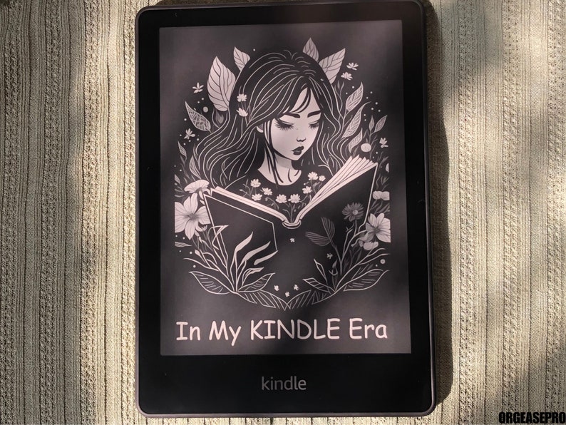 May include: A black and white illustration of a woman reading a book on a Kindle e-reader. The illustration is surrounded by flowers and leaves. The text on the screen reads "In My Kindle Era".