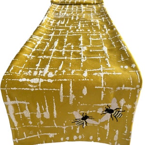 May include: A yellow table runner with a white geometric pattern and two embroidered bees.