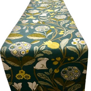 May include: A white ceramic mug with a black handle and the text "But First, Coffee" in a bold, black font. The mug is set against a blurred background. The mug appears to be approximately 10 cm tall.