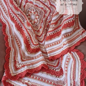 Op de afbeelding: Een handgemaakte gehaakte deken in tinten koraal, crème en beige. De deken heeft een gedetailleerd bloemmotief in het midden en een geschulpte rand. De tekst "One Stitch at a Time Crochet" is rechtsboven zichtbaar.