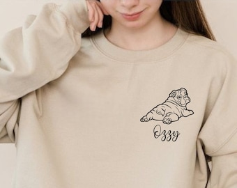 May include: A beige sweatshirt with a black outline of a bulldog lying down and the name "Ozzy" printed below it.