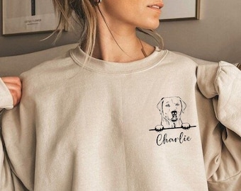 May include: A beige sweatshirt with a black graphic of a Labrador Retriever peeking over the top with the name "Charlie" underneath.