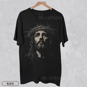 May include: Black t-shirt featuring a sepia-toned portrait of Jesus wearing a crown of thorns. The image is centered on the shirt, with the text "MELYAPParel" printed at the top and bottom. The word "BLACK" is printed at the bottom.