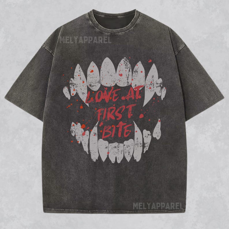 K&ouml;nnte beinhalten: Dunkelgraues T-Shirt mit einem verwitterten Aufdruck eines Mundes mit scharfen Z&auml;hnen und den Worten "LOVE AT FIRST BITE" in Rot. Das Shirt hat einen Vintage-Look und der Markenname "MELYAPPAREL" ist oben aufgedruckt.