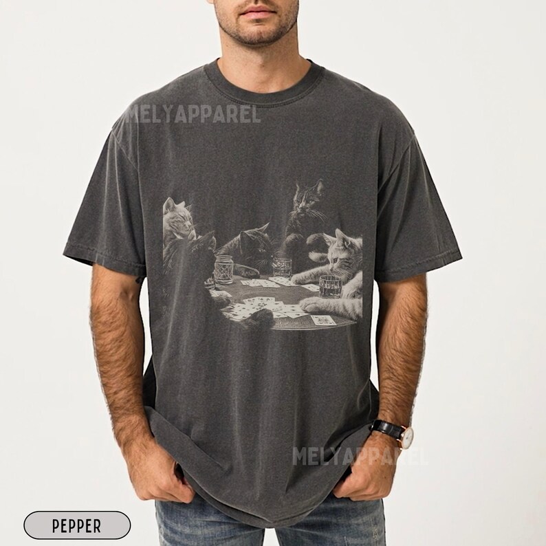 Puede incluir: Camiseta color pimienta con un gr&aacute;fico en blanco y negro de gatos jugando al p&oacute;quer. La imagen muestra cinco gatos alrededor de una mesa de p&oacute;quer con cartas y vasos. La camiseta tiene un aspecto vintage y desgastado y el texto "MELY APPAREL" est&aacute; impreso.