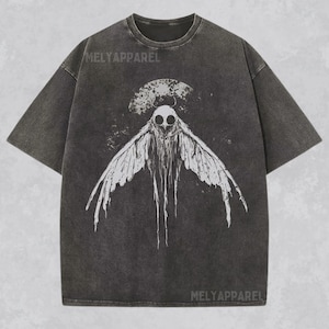 May include: A dark gray t-shirt with a white graphic print of a moth with large eyes and wings. The text "MELYAPPAREL" is printed on the shirt.
