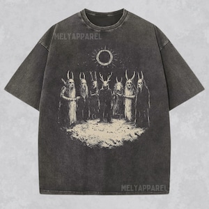 May include: A black t-shirt with a vintage-style graphic print of a group of figures with horns and a sun with a circle in the middle. The text "MELYAPPAREL" is printed on the shirt.