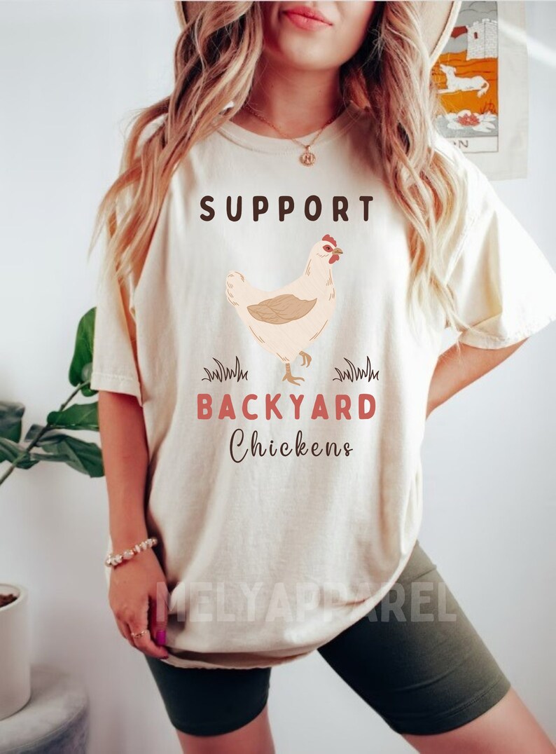 以下が含まれることがあります： 「SUPPORT BACKYARD CHICKENS」という文字と、鶏の漫画の絵が描かれた白いTシャツです。