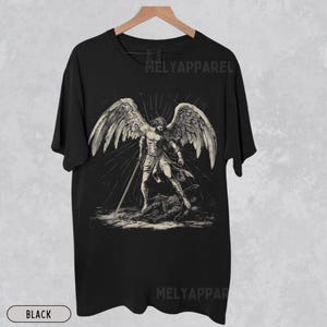 May include: Black t-shirt with a monochrome illustration of an angel with large wings and a sword. The design includes the text "MELYAPPPAREL". The word "BLACK" is printed at the bottom. The image is on a neutral background.