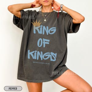 May include: A dark gray oversized t-shirt with a blue and gold graphic that says "King of Kings" and "Revelation 19:16".