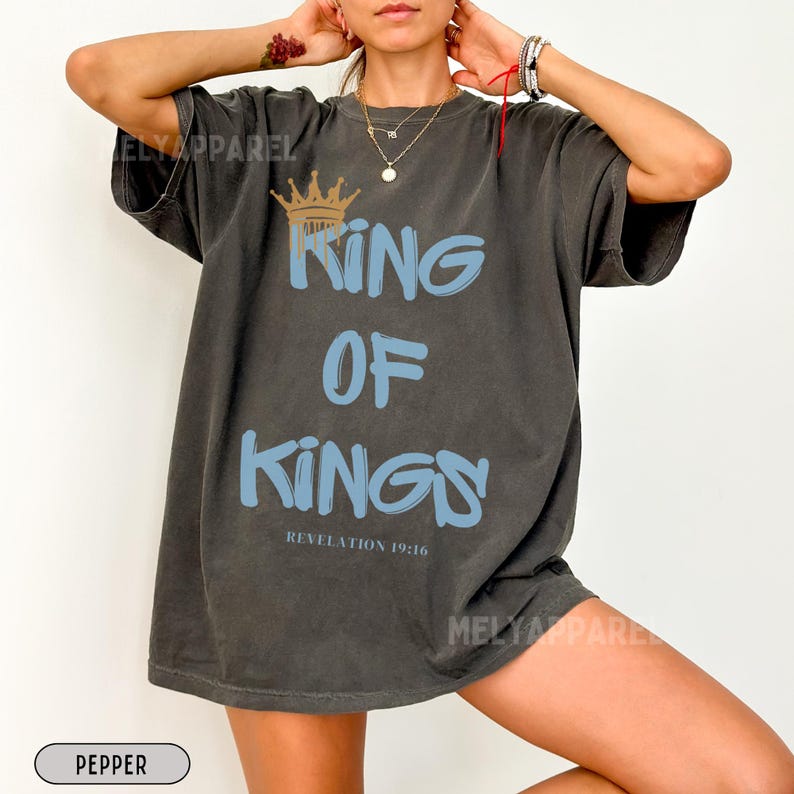 May include: A dark gray oversized t-shirt with a blue and gold graphic that says "King of Kings" and "Revelation 19:16".