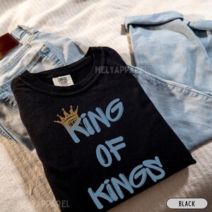 May include: Black t-shirt with a blue and gold crown and the text "King of Kings" in blue.
