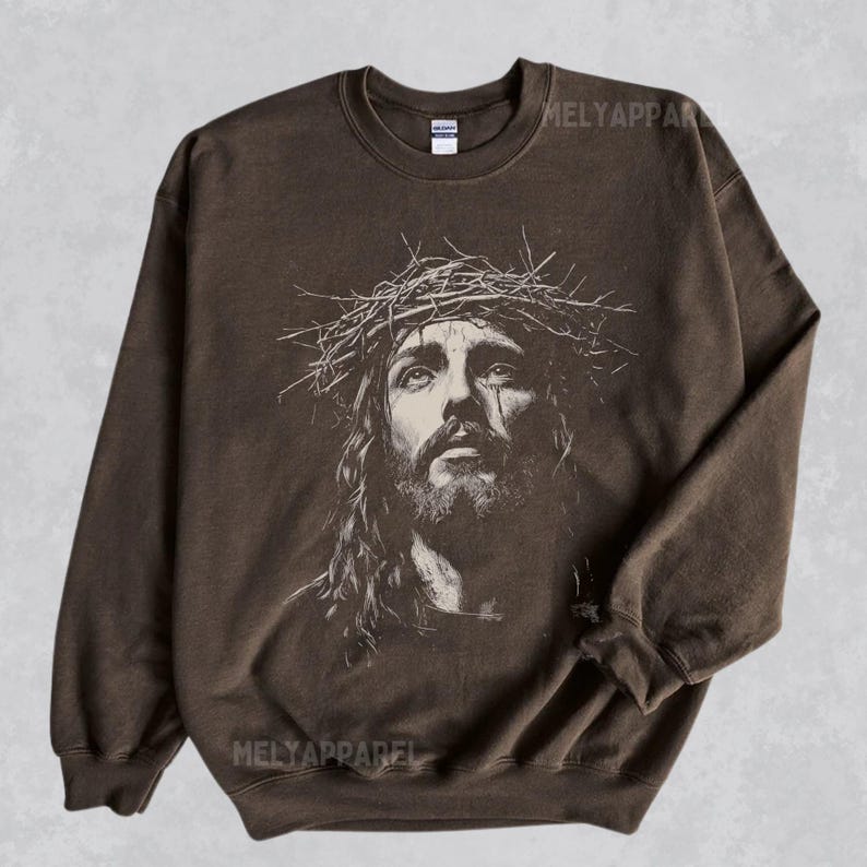 May include: Brown crewneck sweatshirt featuring a black and white portrait of Jesus wearing a crown of thorns. The image is centered on the front of the sweatshirt. The text "MELYAPPAREL" is printed on the top and bottom of the sweatshirt.