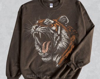 May include: A brown sweatshirt with a graphic print of a roaring tiger. The tiger is facing the right side of the image and has a white and orange striped pattern. The sweatshirt has a crew neck and long sleeves.