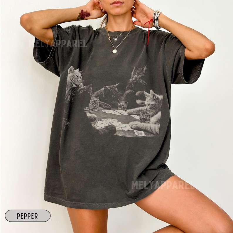 Puede incluir: Camiseta gris oscuro con un gr&aacute;fico en blanco y negro de gatos jugando al p&oacute;quer. La camiseta tiene el texto "ELY APPAREL" y "MELY APPAREL" impreso. La palabra "PEPPER" est&aacute; impresa en un &oacute;valo blanco en la parte inferior.