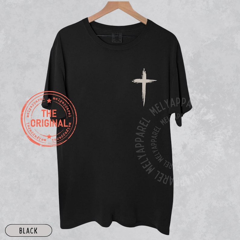 May include: Black t-shirt with a white cross graphic on the front. The shirt has the text "THE ORIGINAL" and "MELYAPPAREL" printed on it. The word "BLACK" is printed at the bottom of the shirt.