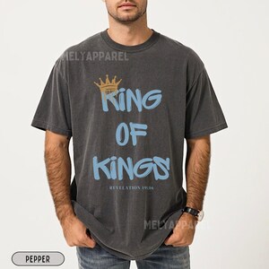 May include: A black t-shirt with a graphic print of a crown and the text "King of Kings" in blue and gold. The text "Revelation 19:16" is printed below the graphic.