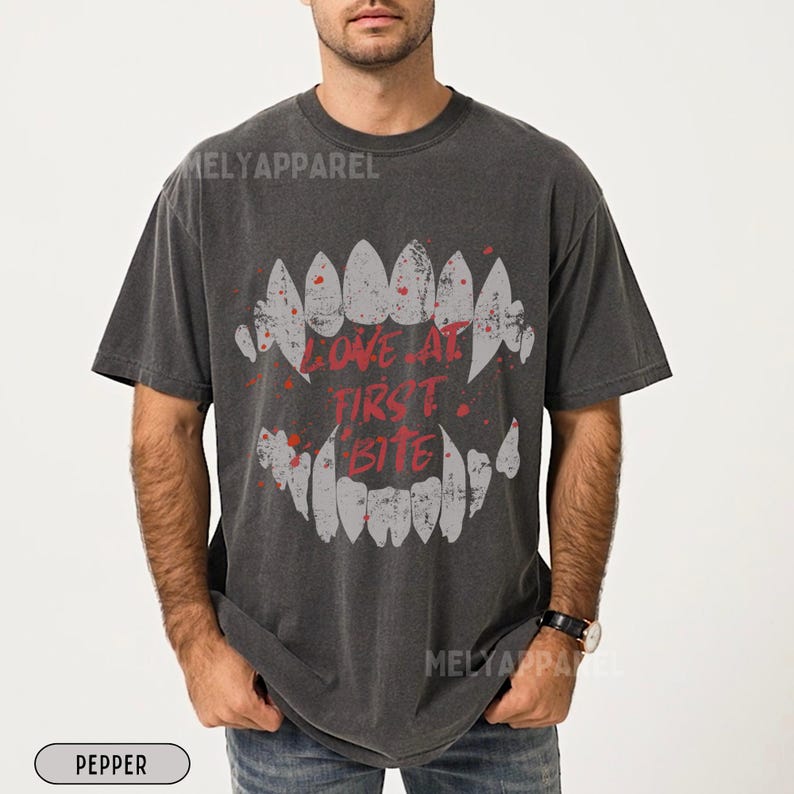 K&ouml;nnte beinhalten: Dunkelgraues T-Shirt mit einem grafischen Motiv aus stilisierten Z&auml;hnen und dem roten Schriftzug "LOVE AT FIRST BITE". Das Design hat einen Used-Look und wirkt vintage.