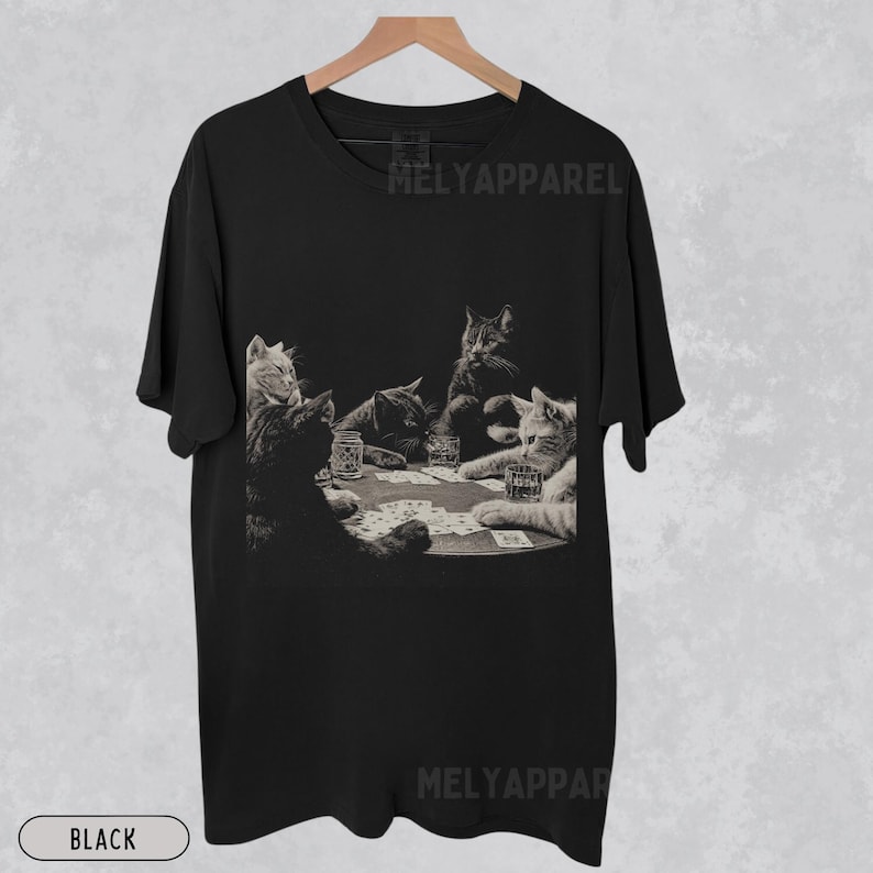 Puede incluir: Camiseta negra con un gr&aacute;fico en tonos sepia de gatos jugando al p&oacute;quer alrededor de una mesa. La imagen incluye vasos de whisky y naipes. El texto "MELYAPPAREL" est&aacute; impreso en la camiseta. La palabra "BLACK" est&aacute; impresa en la parte inferior.