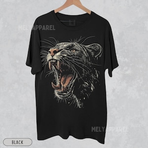 May include: Black t-shirt with a graphic print of a roaring black panther. The panther's mouth is open, showing its teeth and tongue. The graphic is detailed and realistic.