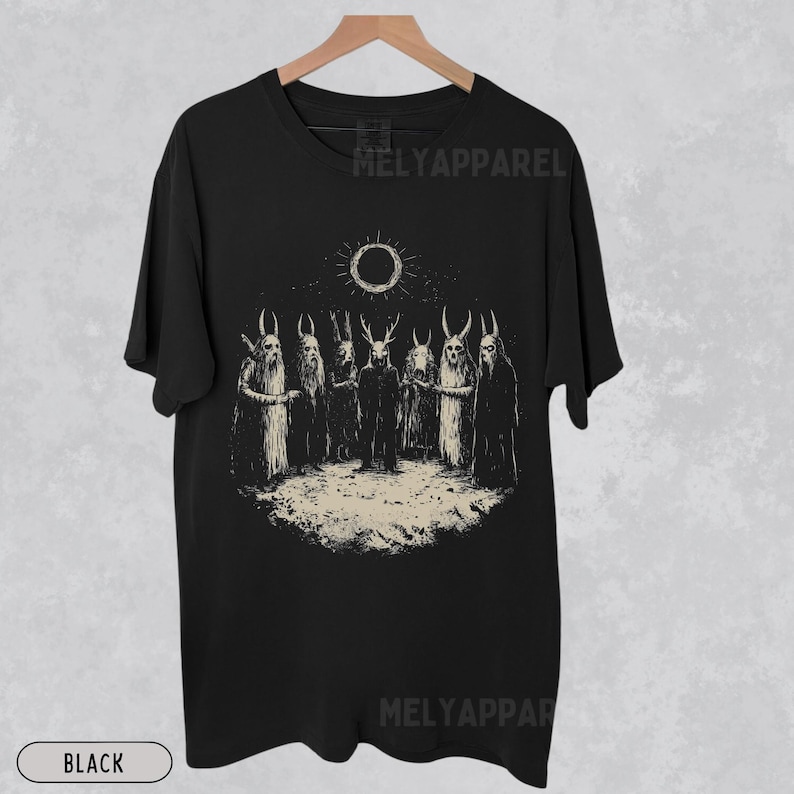 May include: Black t-shirt featuring a graphic print of a group of figures with horns and a sun with a black circle in the centre. The text "Melyapparel" is printed on the shirt.