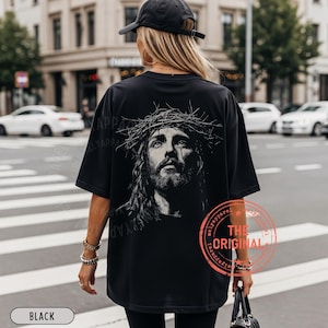 May include: Black oversized t-shirt featuring a detailed black and white portrait of Jesus wearing a crown of thorns. The shirt has the text "THE ORIGINAL" in a red circle. The word "BLACK" is in a white rectangle at the bottom.