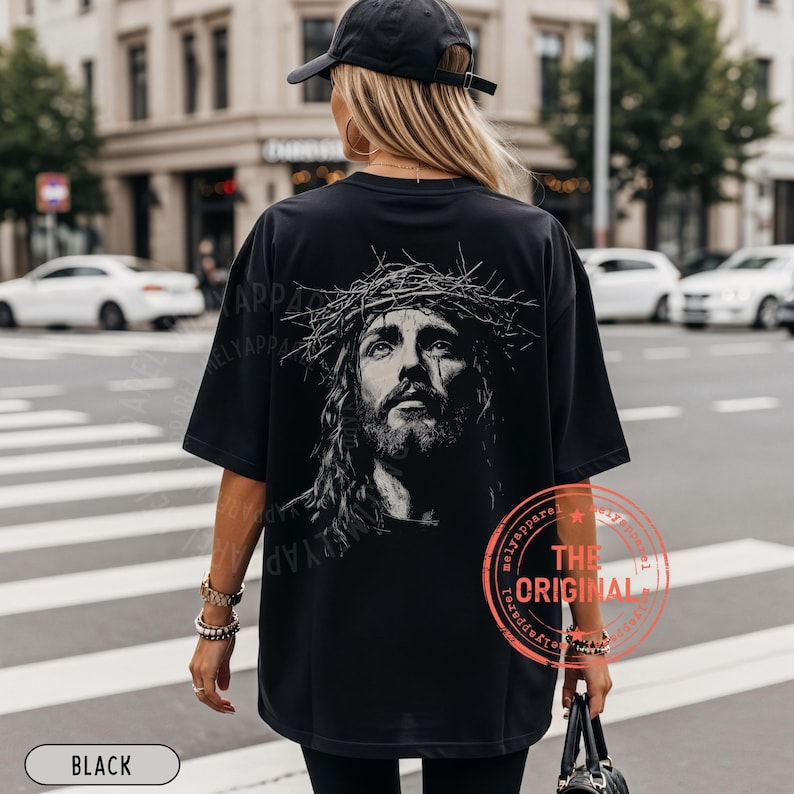 May include: Black oversized t-shirt featuring a detailed black and white portrait of Jesus wearing a crown of thorns. The shirt has the text "THE ORIGINAL" in a red circle. The word "BLACK" is in a white rectangle at the bottom.