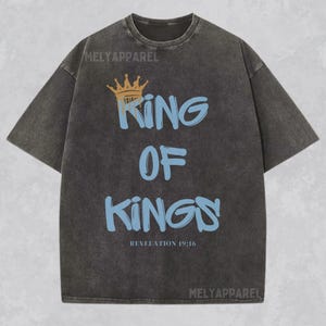 May include: A black t-shirt with a faded look features a gold crown and the text "King of Kings" in blue with a graffiti style font. The text "Revelation 19:16" is printed below the main text.