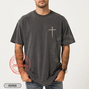 May include: Pepper-colored t-shirt with a cross and nail design. The shirt features the text "MELYAPPAREL" on the sleeve and a stamp that says "THE ORIGINAL". The word "PEPPER" is printed at the bottom.