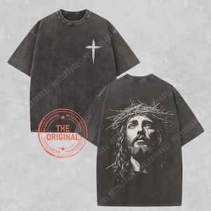 May include: Dark gray t-shirts with a distressed look. One shirt features a white cross on the front, the other a detailed image of Jesus wearing a crown of thorns. The shirts have a vintage style.