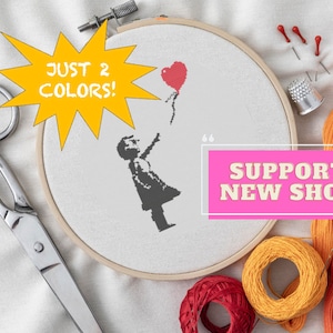 May include: A close-up of a cross-stitch embroidery hoop with a black and white image of a girl reaching for a red heart-shaped balloon. The text "JUST 2 COLORS!" is in a yellow speech bubble. The hoop is surrounded by red, orange, and yellow embroidery floss, a thimble, and sewing pins. The text "SUPPORT NEW SHOP" is in a pink rectangle.