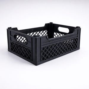 May include: A black plastic crate with a rectangular shape. The crate has a lattice design on the sides and a handle cutout on each end. The crate is designed for storage and transport.