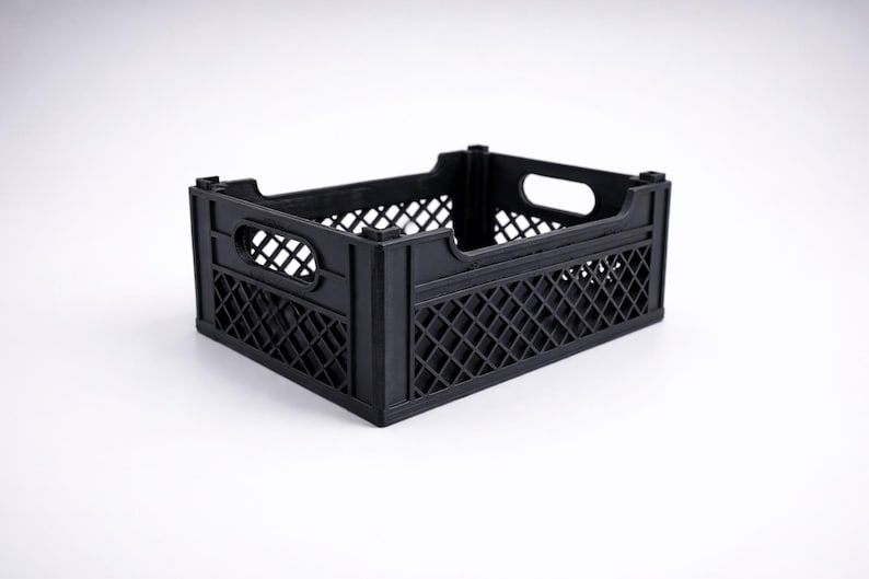 May include: A black plastic storage crate. It features a rectangular shape with a lattice pattern on the sides and handle cutouts. The crate is designed for carrying and storing items.