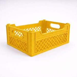 May include: A yellow plastic crate with a rectangular shape. The crate features a lattice design on the sides and handle openings at each end. The crate is designed for storage and transport.