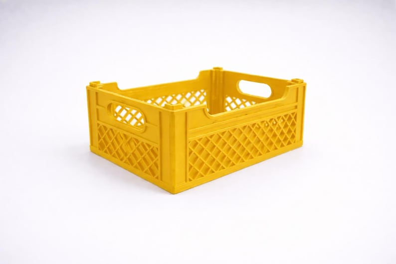 May include: A yellow plastic crate with a rectangular shape. The crate features a lattice design on the sides and handle openings at each end. The crate is designed for storage and transport.