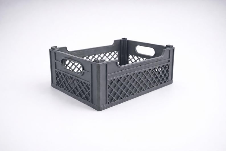 May include: A dark grey plastic crate with a rectangular form. The crate features a lattice pattern on its sides and oval-shaped handles. This storage container is suitable for various items.