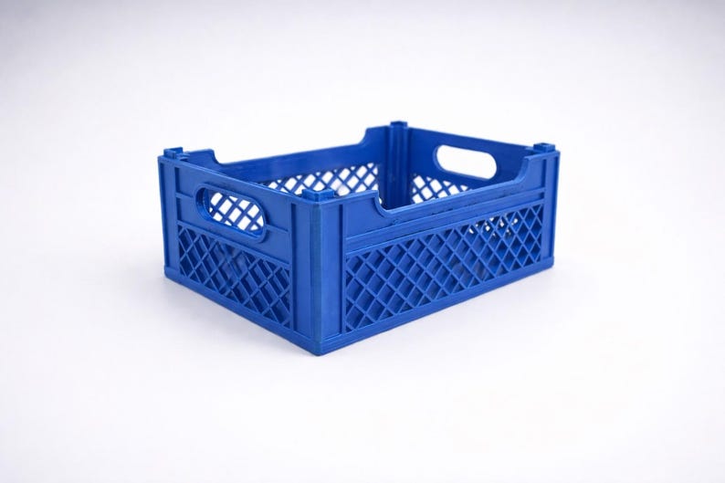 May include: A blue plastic storage crate. It features a lattice pattern on the sides and handle cutouts. The crate is designed for carrying and storing items, with dimensions suitable for various uses.