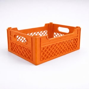 May include: An orange plastic crate. The crate has a rectangular shape with a diamond-patterned design on the sides and handle cutouts. It is empty and sits on a white surface. The crate is likely used for storage.