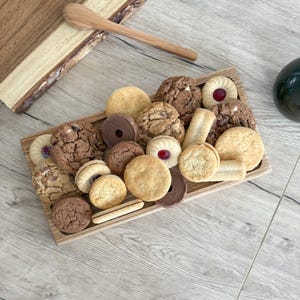 May include: A wooden serving tray filled with a variety of cookies, including chocolate chip, shortbread, and biscuits. The tray is made of natural wood and has a rustic look.
