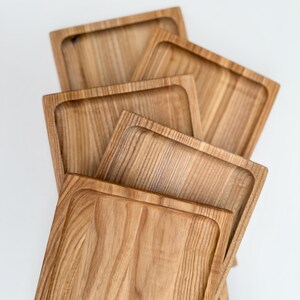 May include: Four wooden serving trays stacked on top of each other. The trays are made of light brown wood with a natural grain pattern. The trays are rectangular in shape and have slightly rounded edges.