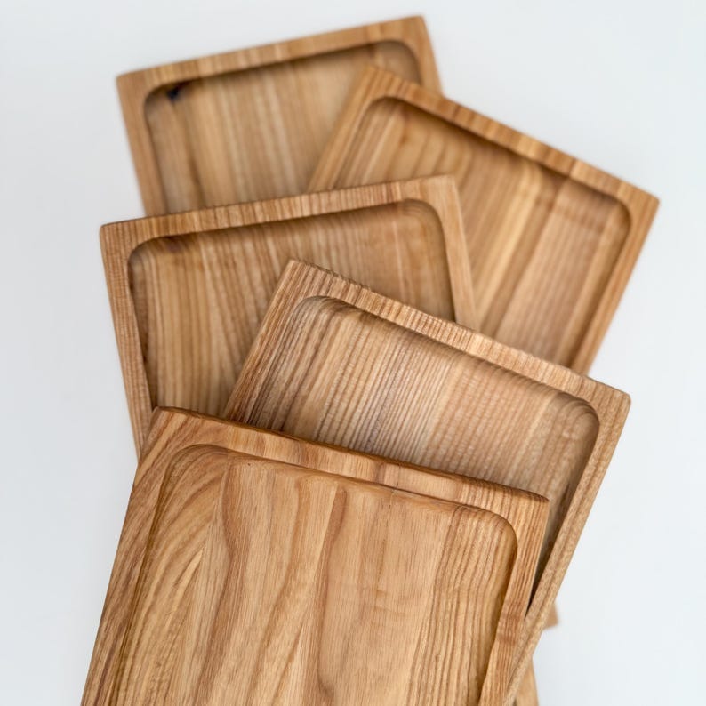 May include: Four wooden serving trays stacked on top of each other. The trays are made of light brown wood with a natural grain pattern. The trays are rectangular in shape and have slightly rounded edges.
