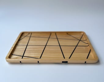 May include: A rectangular wooden tray with a natural wood finish and black lines forming a geometric pattern.
