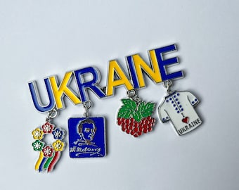 May include: A silver charm bracelet with a blue and yellow enamel charm that says "UKRAINE". The bracelet also has charms of a sunflower, a portrait of a man, a red berry cluster, and a white embroidered shirt with a red heart that says "I LOVE UKRAINE".
