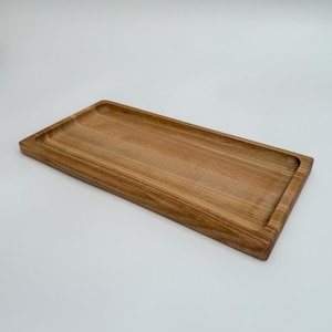 May include: A long, rectangular wooden tray with a slightly raised edge. The tray is made of light brown wood with a natural grain pattern.